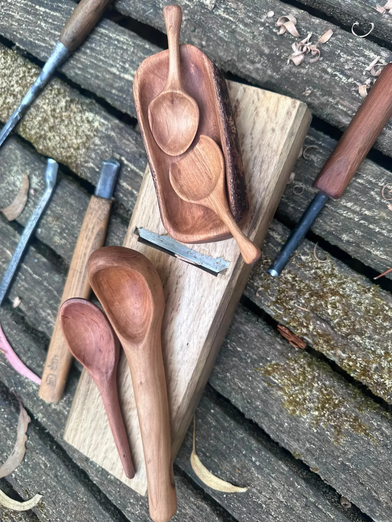 Hand-carved timber spoons and a serving tray beside carving knives and gouges