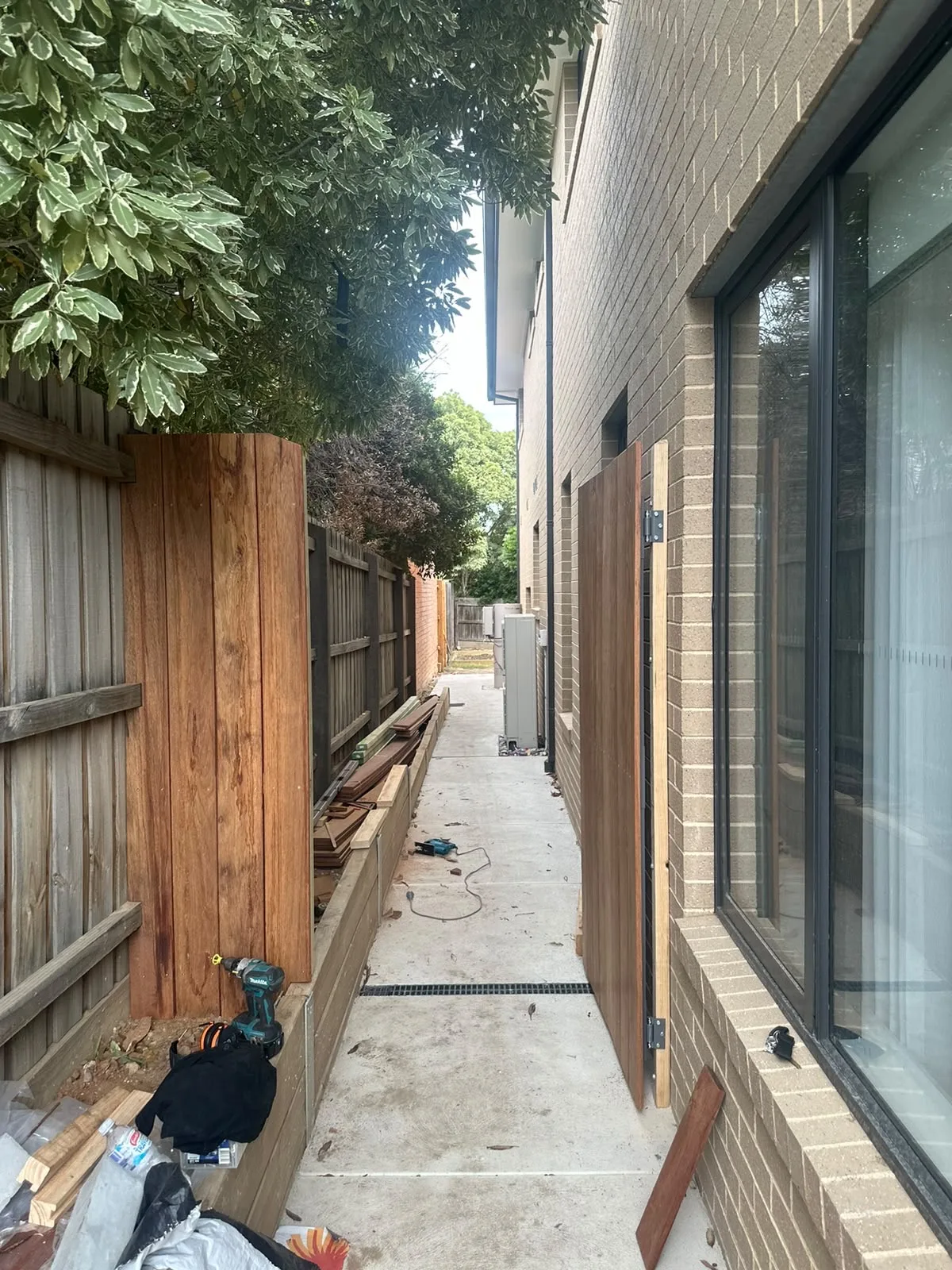 Hardwood side gate and fence panel being hung along a narrow side path beside a brick home