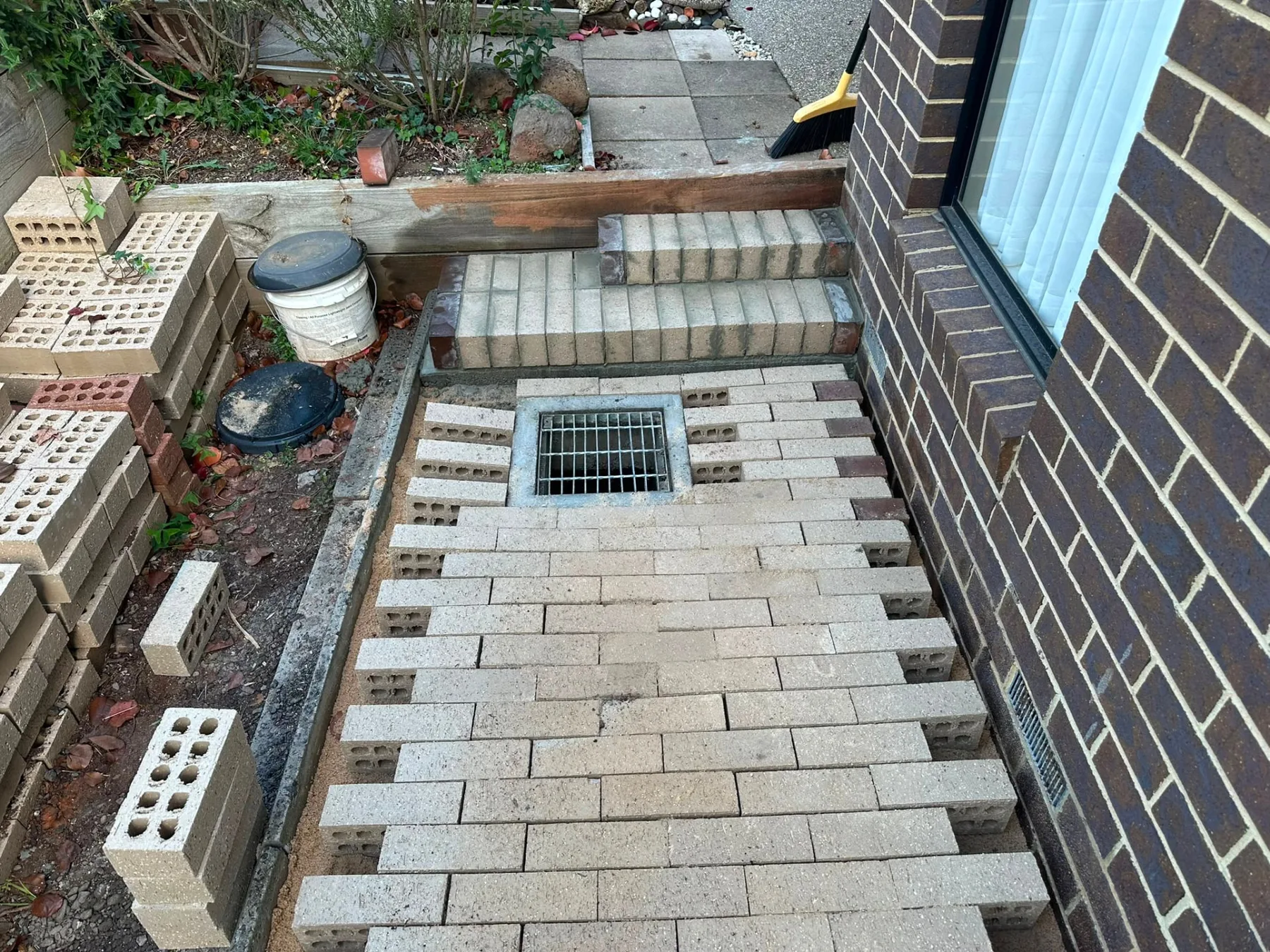 New brick paving and steps laid to fall toward a stormwater grate beside a brick house