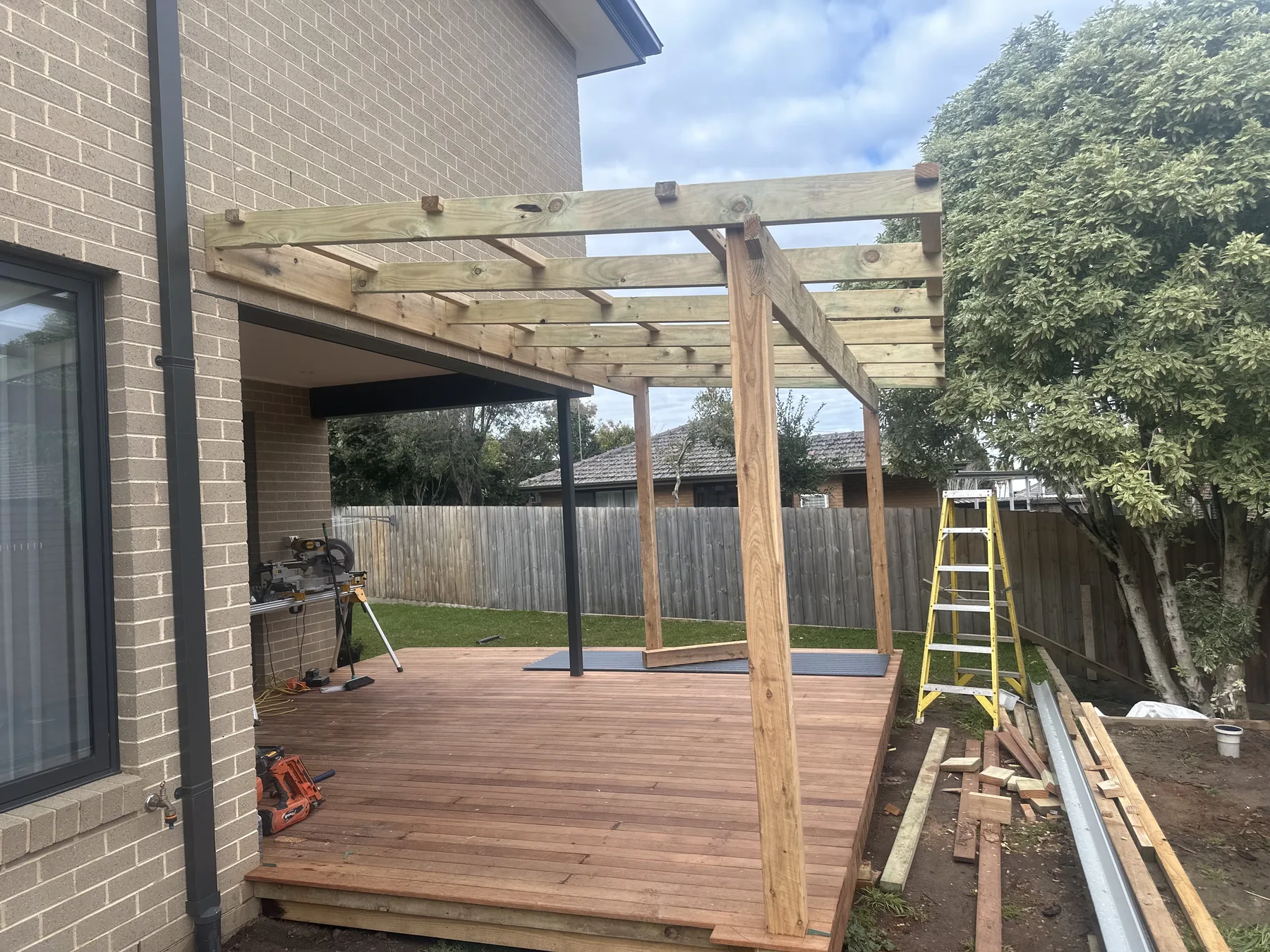 Timber pergola frame completed over a freshly laid hardwood deck beside a brick house