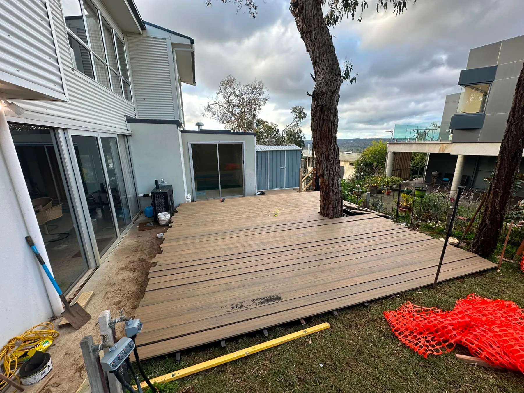 Wide composite deck laid around an established gum tree beside a rendered two-storey home