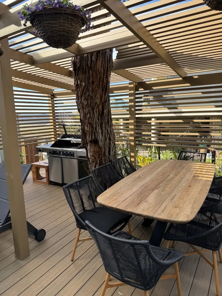 Slatted pergola over a composite deck with an outdoor dining setting and a gum tree growing through