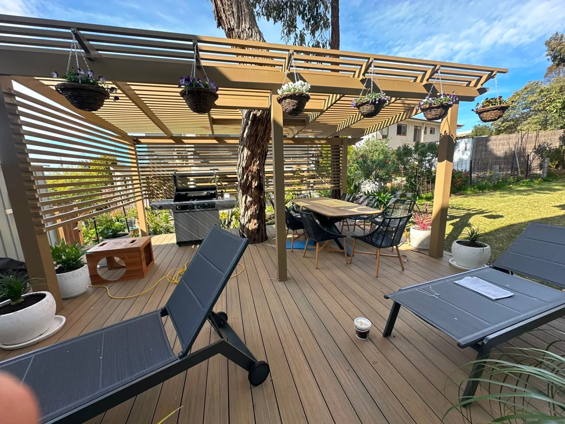Finished slatted pergola over a composite deck built around a mature gum, with dining setting and hanging baskets