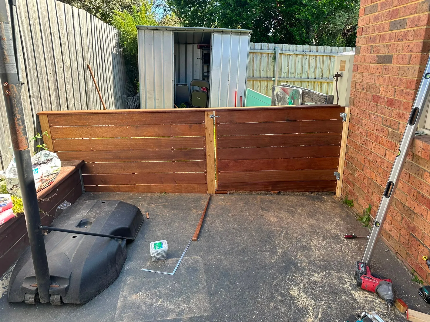 Horizontal merbau privacy screen and matching gate enclosing a courtyard beside a brick house