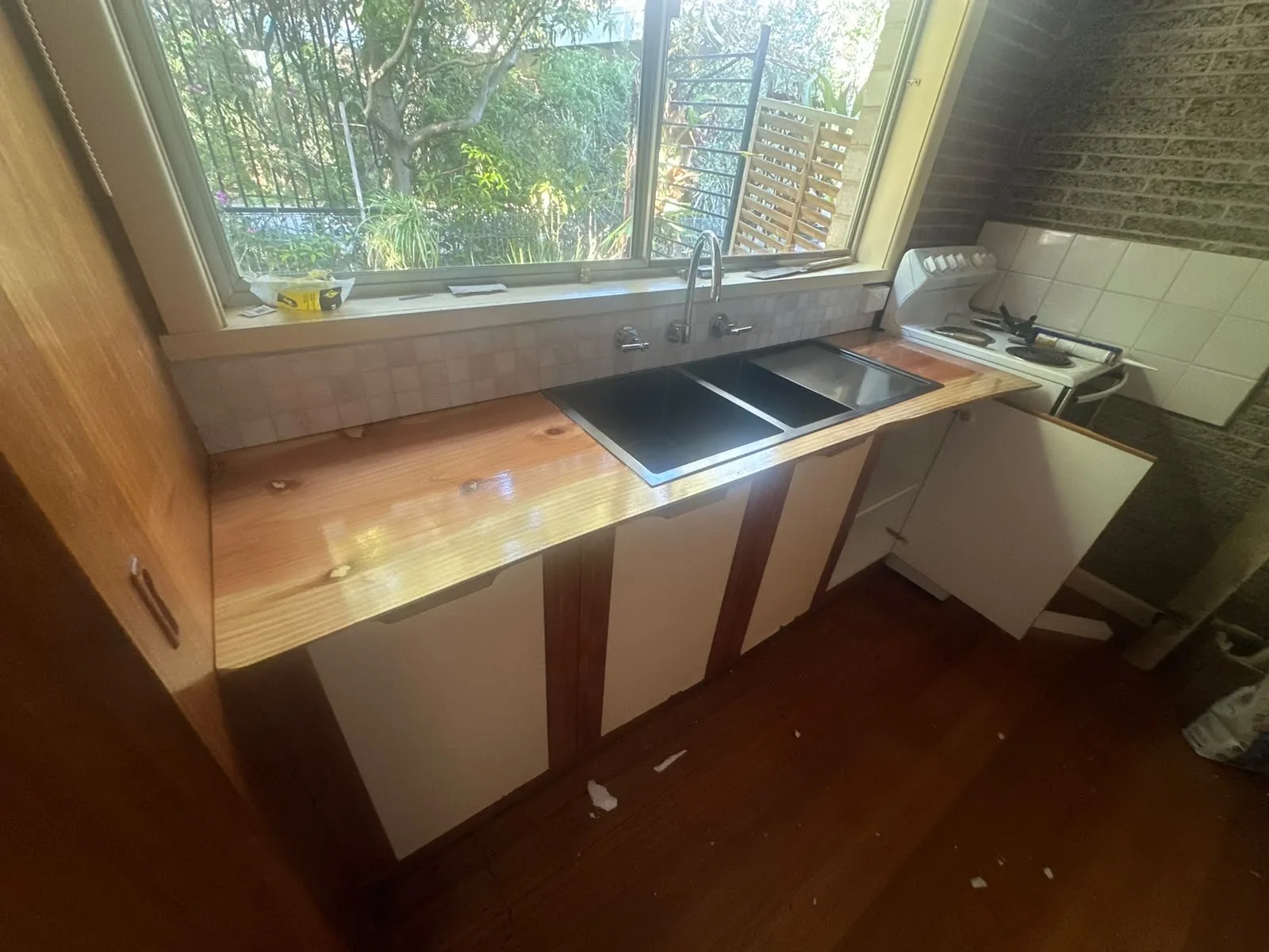 Solid timber kitchen benchtop installed under a window with a black sink and cabinetry below