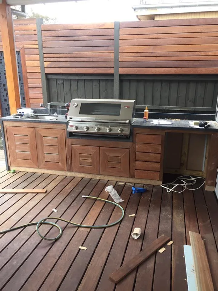 Built-in outdoor kitchen with hardwood cabinetry, stone benchtop and slatted screen behind the barbecue
