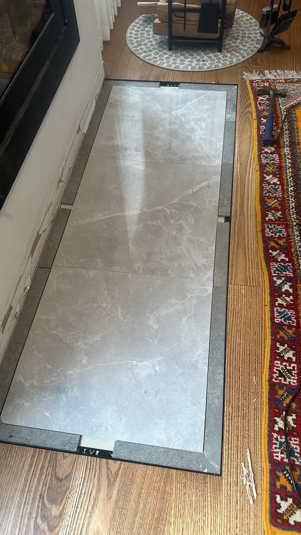 Close detail of a stone-look tiled hearth with mitred border tiles set into timber flooring