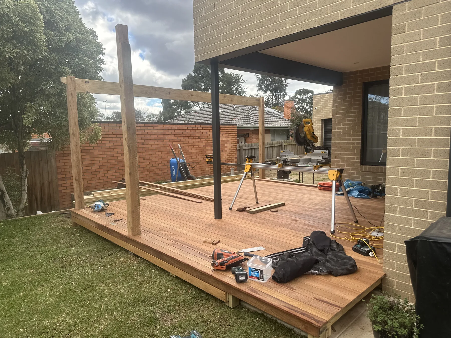 New hardwood deck laid against a brick home with the pergola posts and beams framed up over it