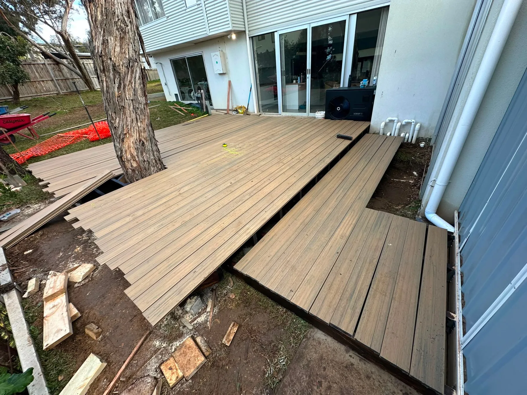Composite decking boards being laid over a level subframe against a rendered home