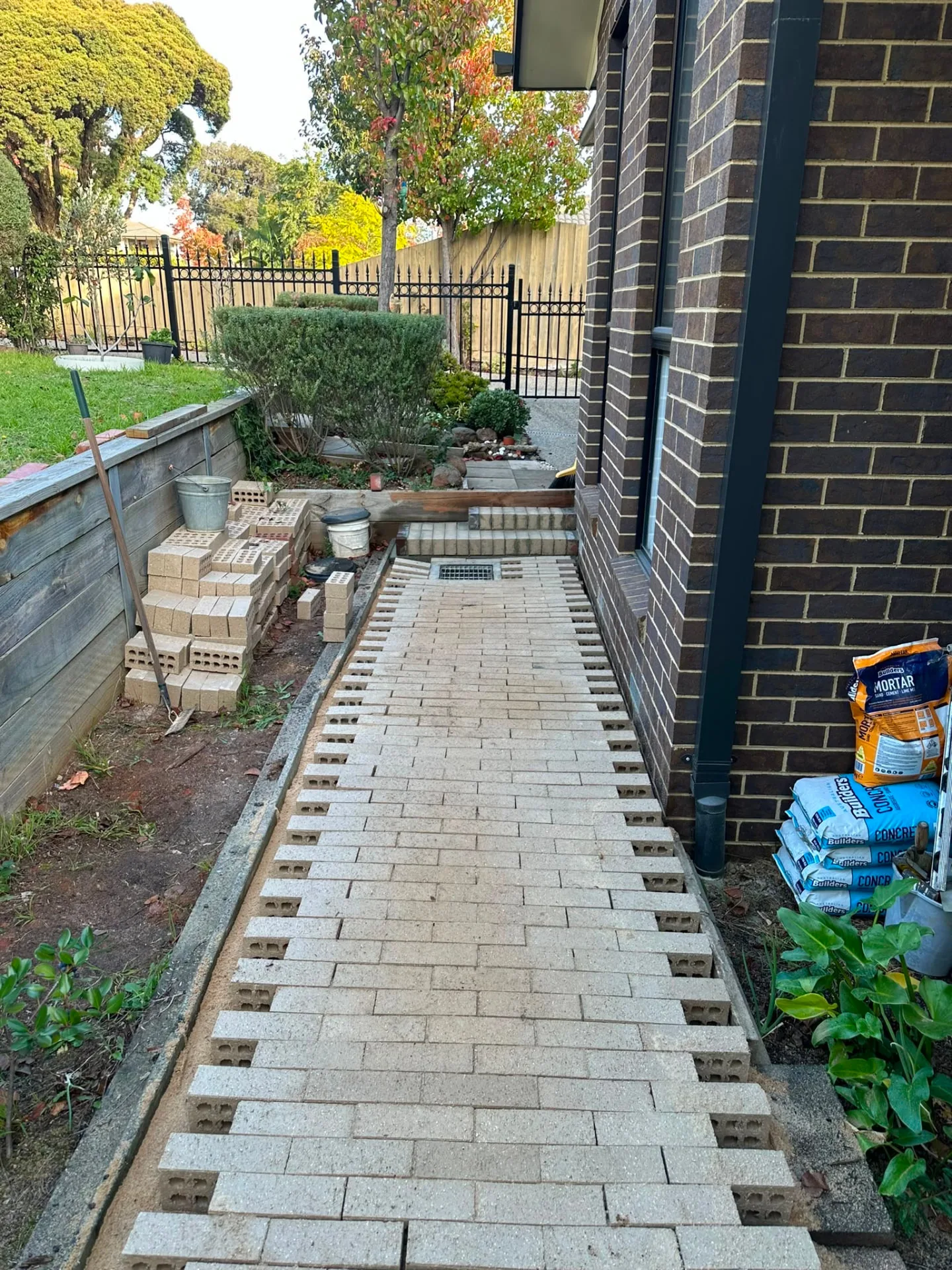 Paver path laid along the side of a brick home with a soldier-course border and stormwater grate