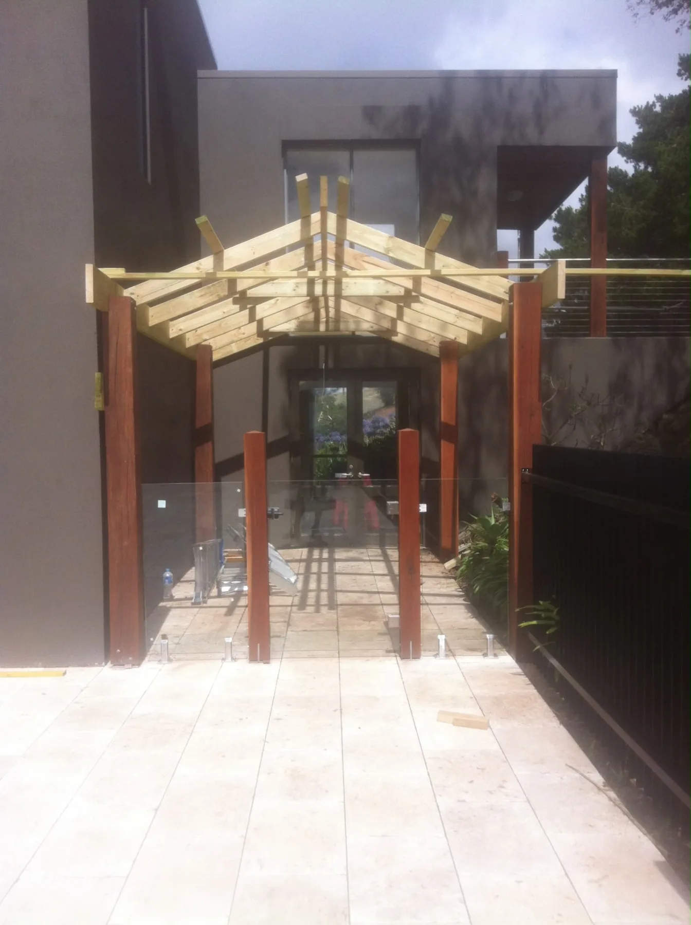 Gabled pergola on hardwood posts framing a paved entry path and glass balustrade