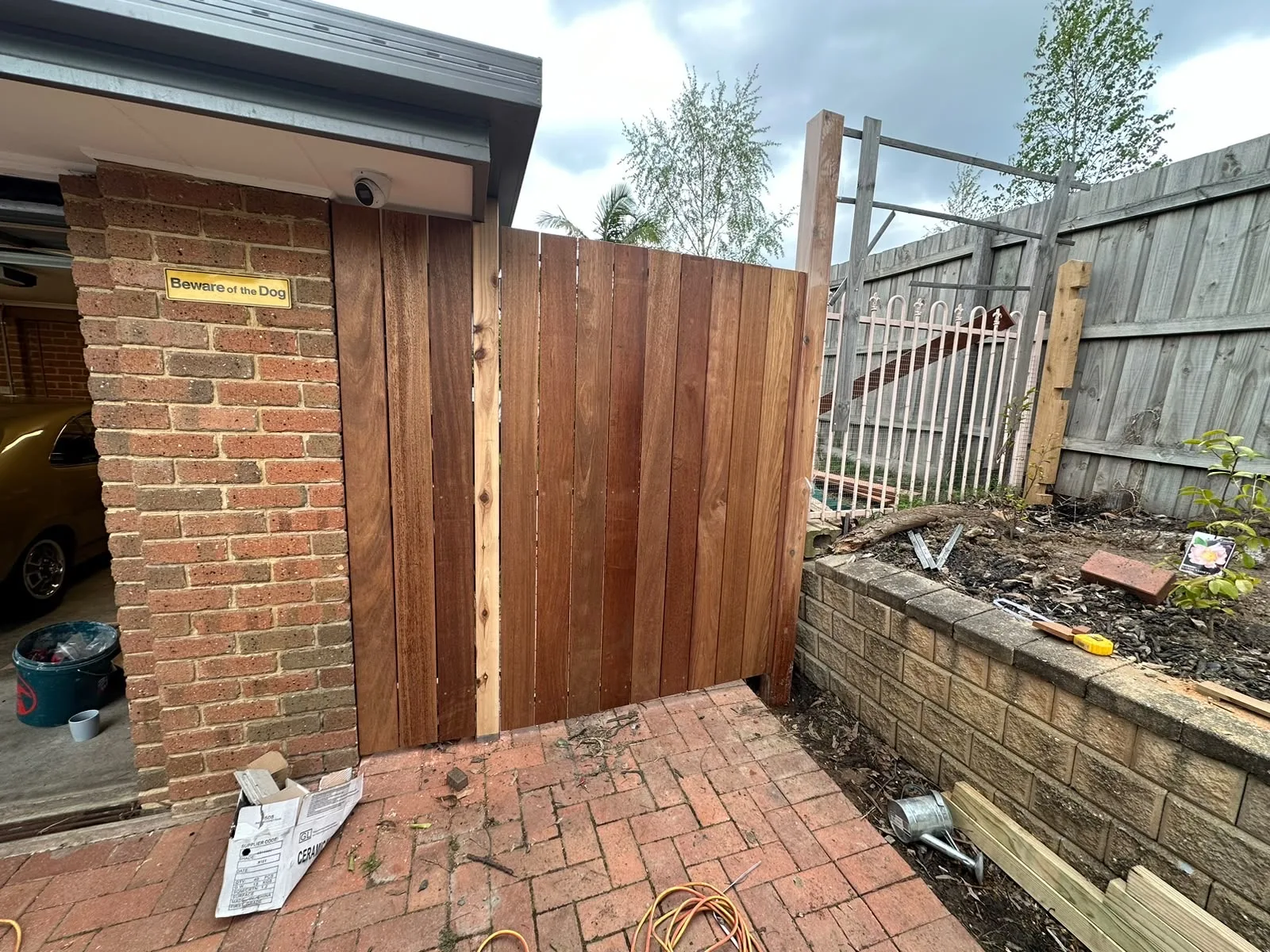 Vertical hardwood gate and fence panel built between a brick garage and a garden retaining wall