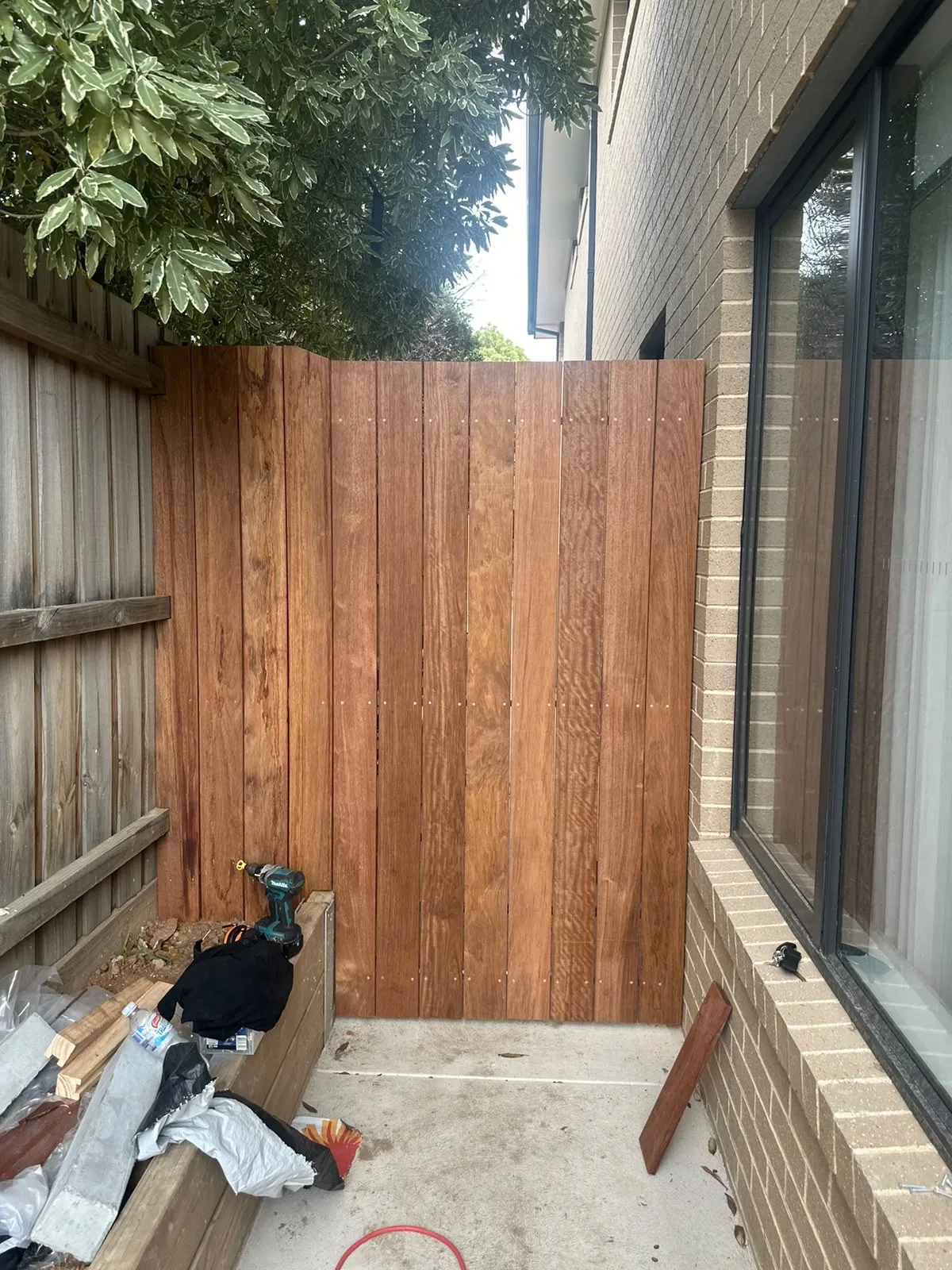 Tall vertical hardwood privacy screen built into a narrow side path against a brick wall