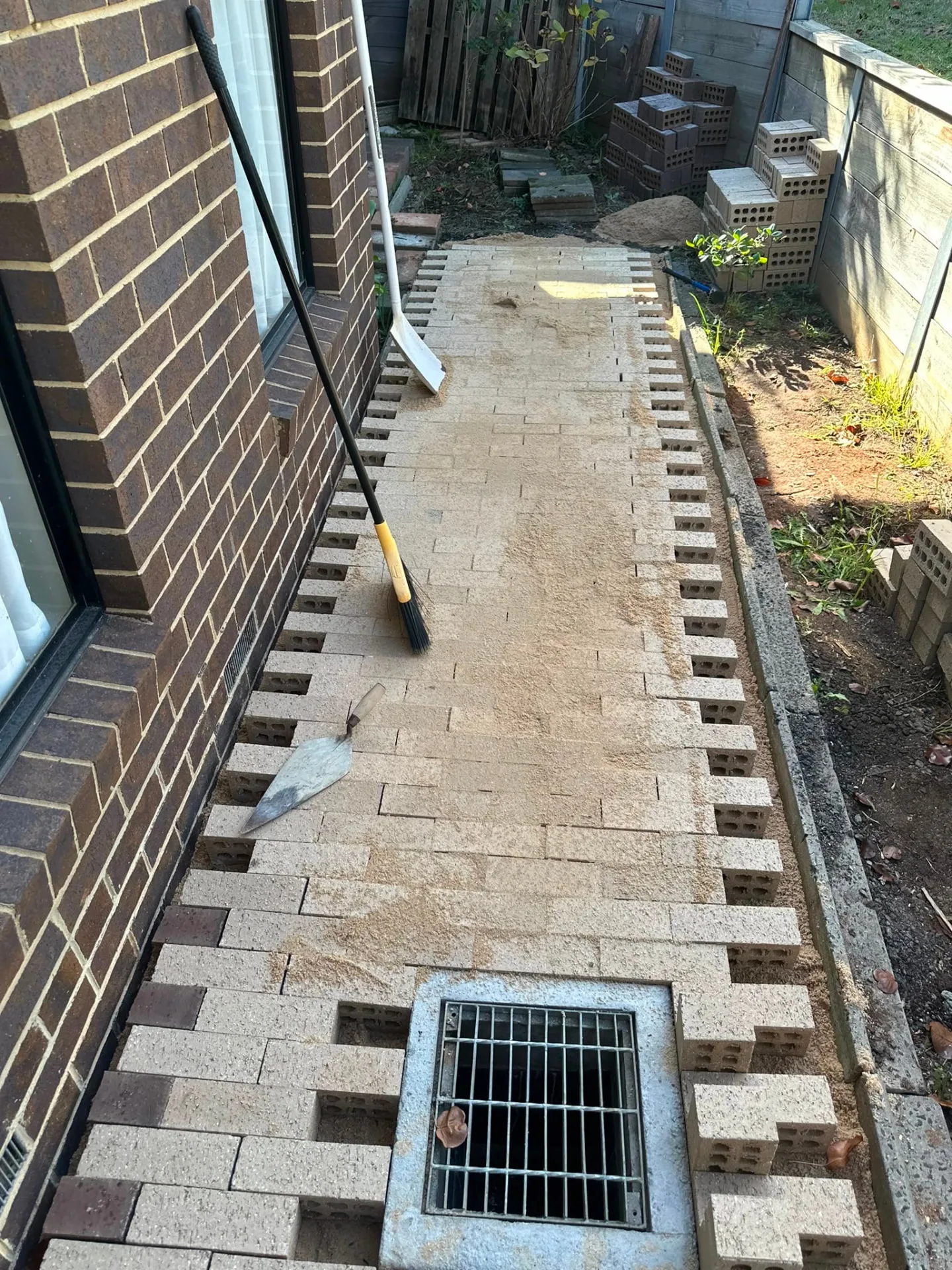 Brick paver path laid beside a house, edged in soldier course and falling to a stormwater grate