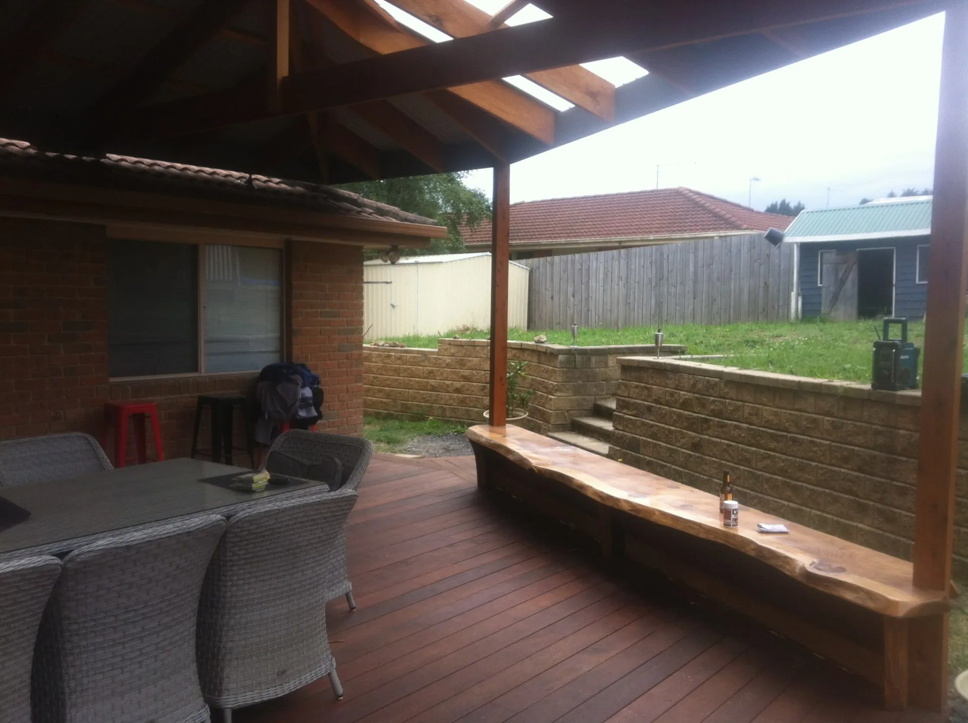 Merbau deck under a timber pergola with a live-edge bench seat running along the retaining wall