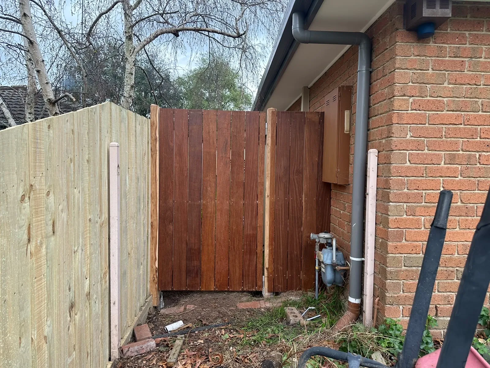 Merbau side gate and privacy screen built alongside a brick house and gas meter