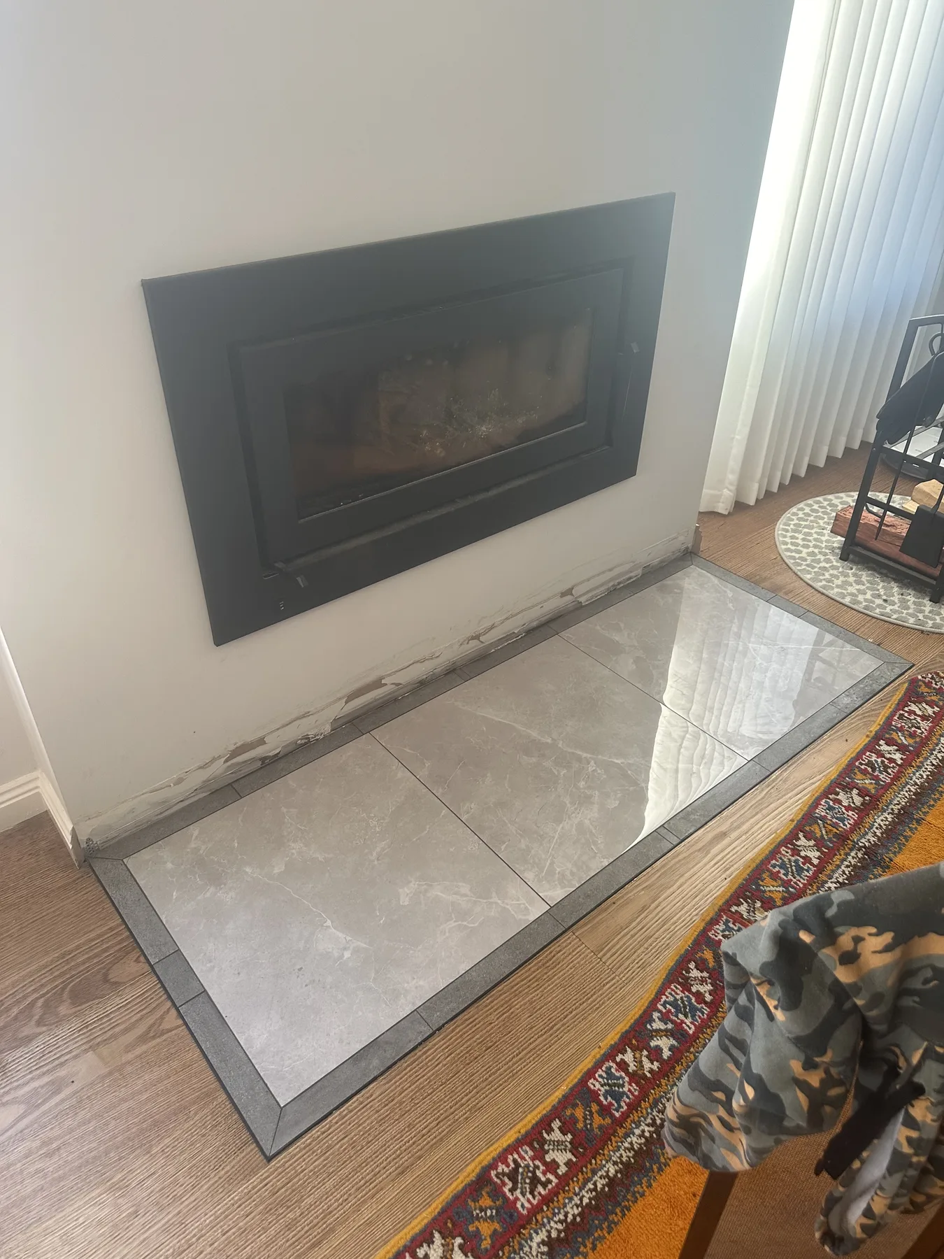 Large-format stone-look tiled hearth laid in front of a wood heater with a contrasting border